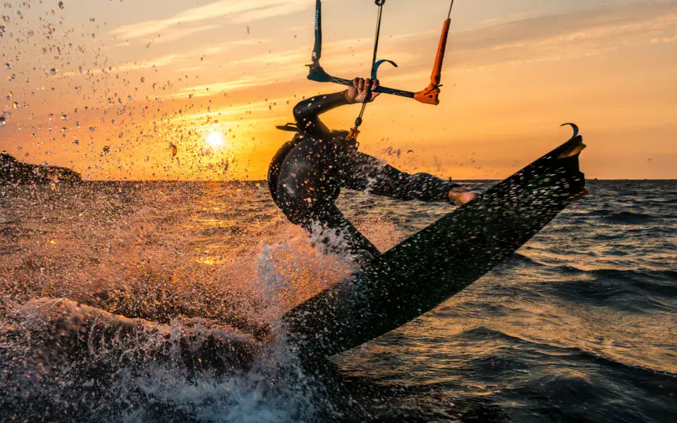 Un kitesurfeur au coucher du soleil, dans les embruns