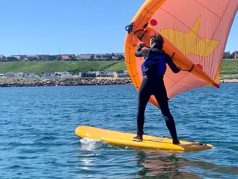 Un élève de wingsurf debout sur sa planche, aile orange en main