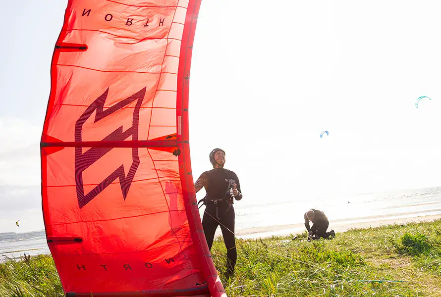Aile de kitesurf rouge posée sur l'herbe près de la côte