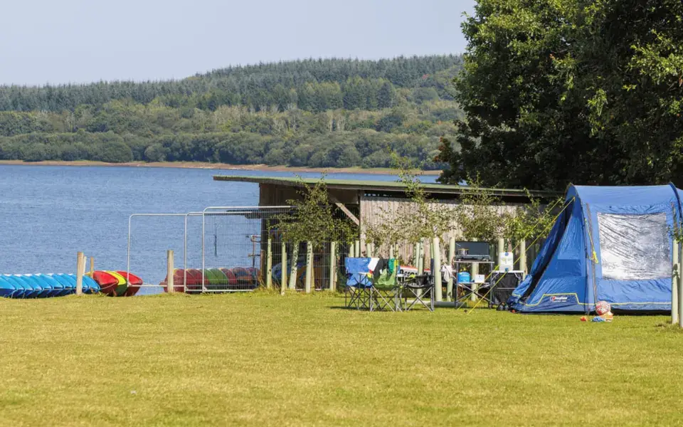 Pelouse au bord d'un lac, avec une tente et du matériel nautique