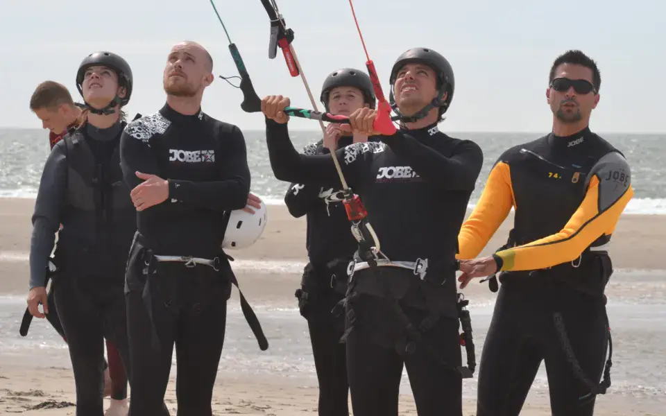 Moniteur et élèves casqués avec une barre de kite sur la plage