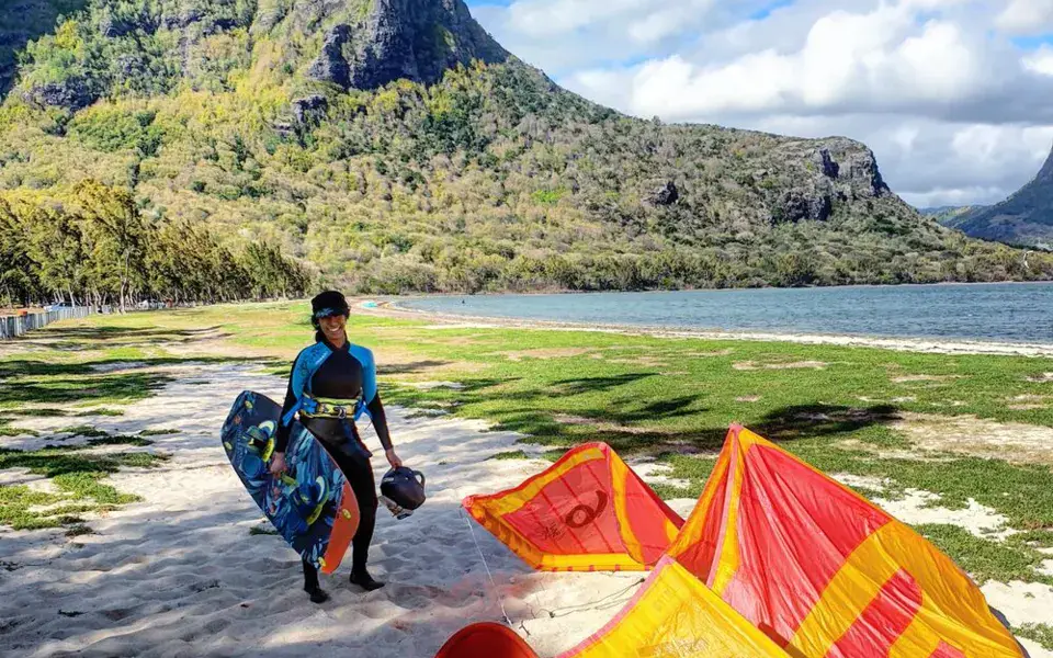 Un kitesurfeur sur la plage avec ses ailes posées au sol, au pied des montagnes