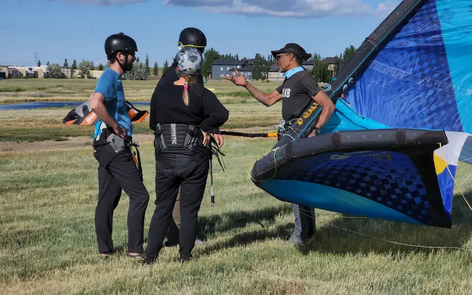 Moniteur expliquant le matériel à des élèves sur une pelouse, aile de kite au sol