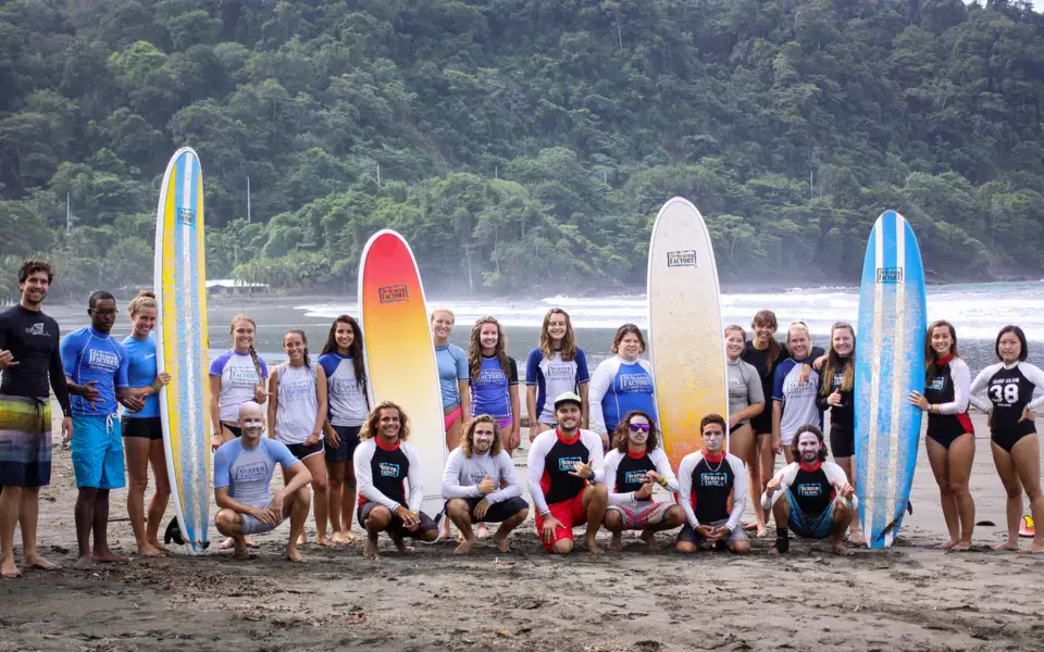 Grand groupe d'élèves et de moniteurs avec leurs planches sur la plage