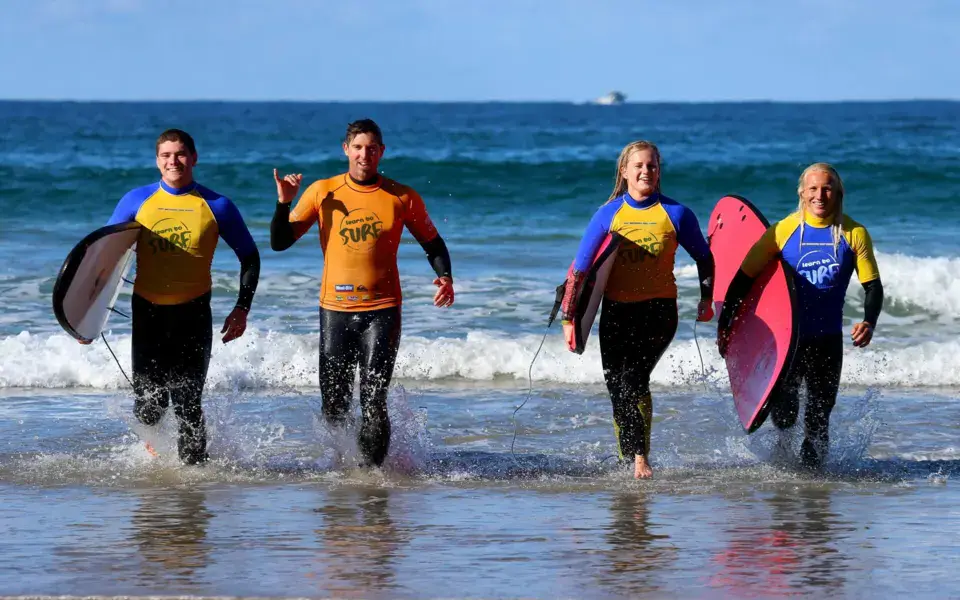 Groupe d'élèves sortant de l'eau avec leurs planches après un cours de surf