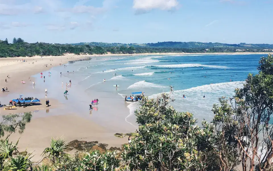 Plage de sable bordée de végétation, baigneurs dans l'eau