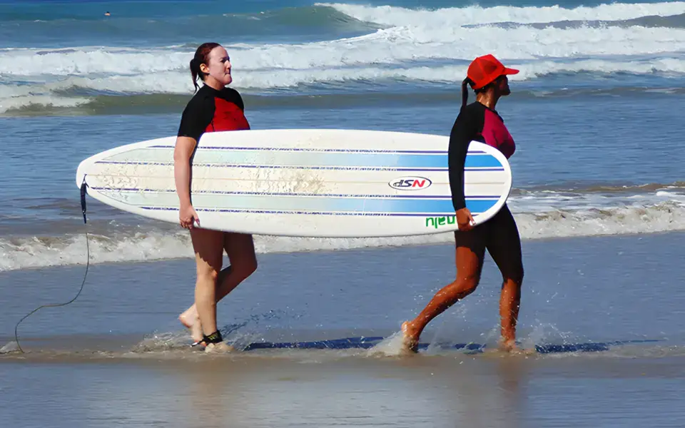 Deux surfeuses portant une planche au bord de l'eau