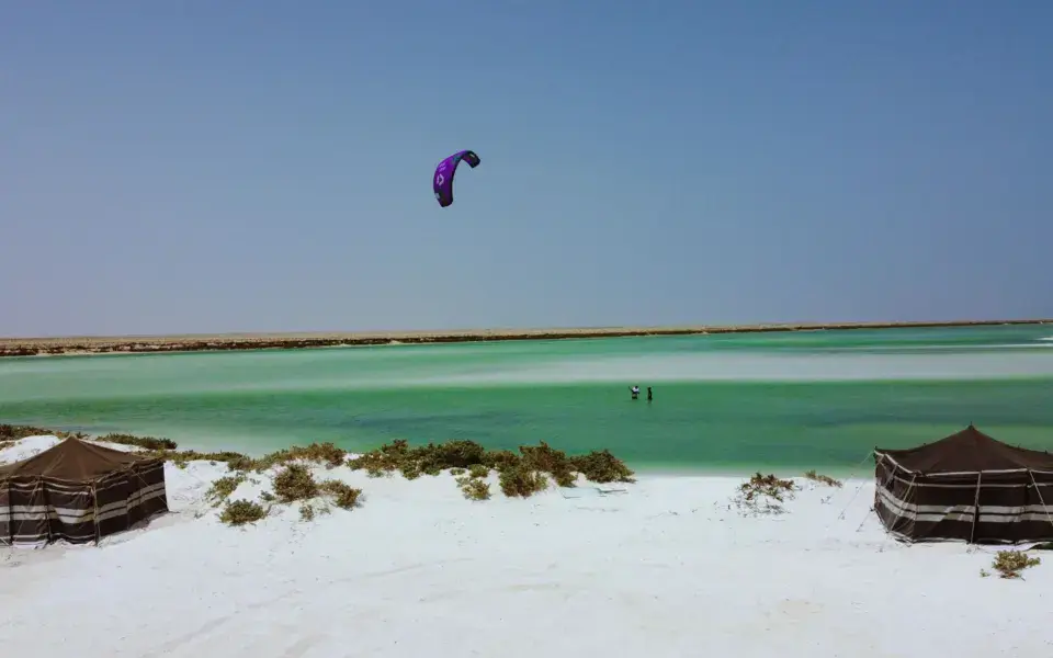 Kitesurfeur au-dessus d'un lagon, avec des tentes de camp sur la plage